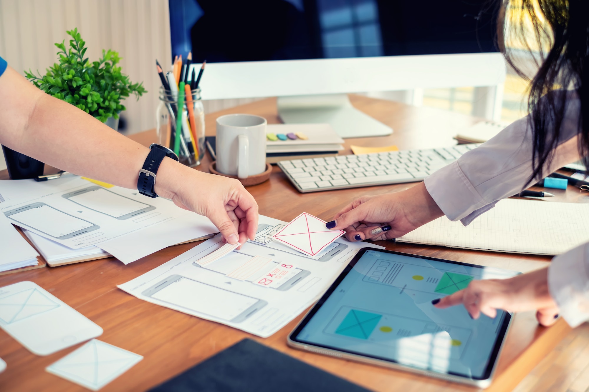 Two female designers drawing a website outline and website ux app development on mobile phone.