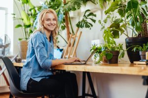 Joyful female business person works on her laptop in office with plants